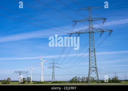 Pilone elettrico e linee elettriche con turbine eoliche nel sfondo Foto Stock