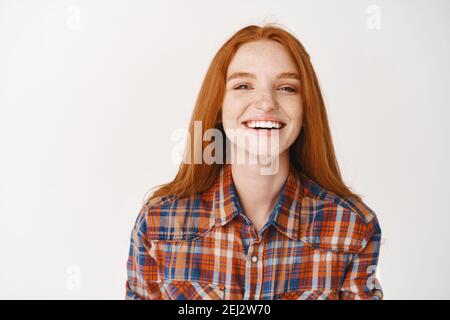 Studente di ragazza con i capelli di zenzero e gli occhi blu sorridenti felici alla macchina fotografica. Giovane donna rossa in piedi allegra su sfondo bianco Foto Stock