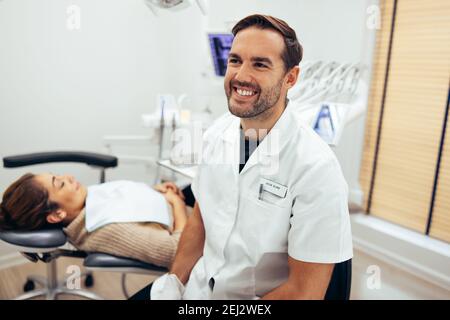 Sorridente dentista maschile nella sua clinica con una paziente femminile in sedia. Dentista maschile nel suo studio dentistico. Foto Stock