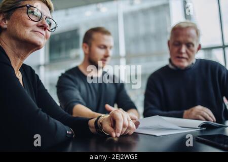 Donna d'affari anziana seduto al tavolo con i colleghi oltre a leggere i documenti contrattuali. Uomini d'affari durante una riunione in ufficio. Foto Stock