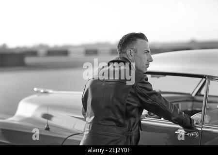 Vista posteriore di un uomo elegante con giacca in similpelle accanto alla cadillac d'epoca. Foto Stock