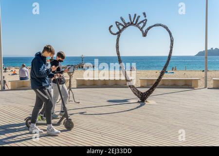 Palmanova, Spagna; febbraio 20 2021: Passeggiata marittima della località turistica maiorchina di Palmanova, con una scultura a cuore di ferro. Adolescenti a piedi Foto Stock