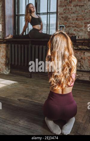 Due amici femminili scattano foto dopo un duro studio di stile loft di workout. Donna fare foto del suo amico flessibile facendo splits sul davanzale Foto Stock