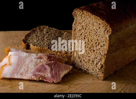 Pane nero e lardo salato con strisce di carne una tavola di legno su sfondo nero Foto Stock