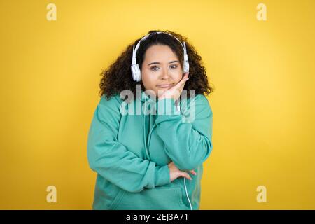 Giovane afroamericana che indossa abiti da palestra e utilizza le cuffie pensare stanco e annoiato con le braccia incrociate Foto Stock