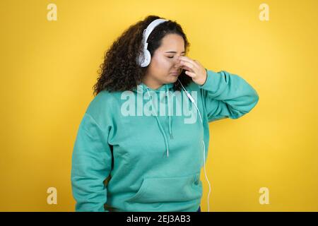 Giovane afroamericana che indossa abiti da palestra e che usa le cuffie puzzava qualcosa di stinoso e disgustoso, odore intollerabile, trattenendo il respiro Foto Stock