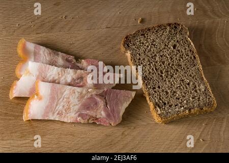 Pane nero e lardo salato con strisce di carne, su tavola di legno Foto Stock