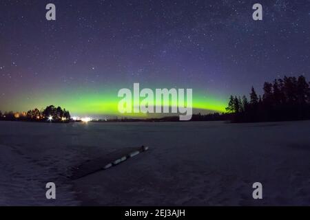 L'aurora borealis polare di notte si illumina nel cielo stellato sopra il lago con l'isola e la silhouette degli alberi vicino alla foresta. Incandescente Foto Stock
