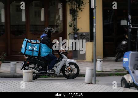 Salonicco, Grecia - Febbraio 20 2021: Corriere alimentare Wolt su moto che velocizza la strada urbana. Vista di giorno del maschio con moto da equitazione casco per consegnare l'ordine di take away contenuto in una scatola del logo dell'azienda Foto Stock