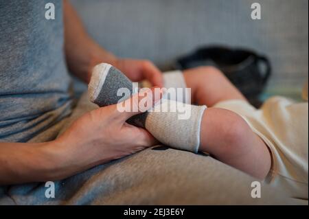 Le mani del padre tengono i piedi del bambino del neonato carino in calze grigie Foto Stock