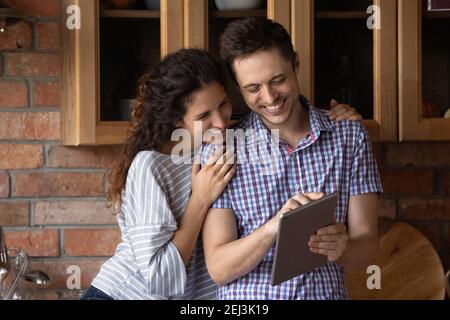 Primo piano su giovane coppia overjoyed usando il tablet in cucina insieme Foto Stock