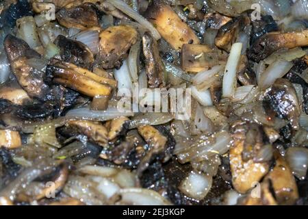 I funghi selvatici con cipolle vengono fritti in una padella. Vendemmia autunnale. Primo piano, messa a fuoco selettiva, texture di superficie. Foto Stock