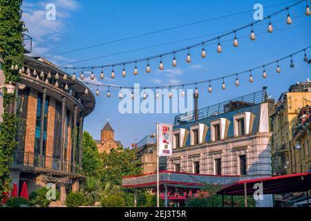 Tbilisi/Georgia – 19 luglio 2019: Paesaggio urbano estivo con architettura moderna e Cattedrale di Sioni all'orizzonte. Lampade garland decorati Foto Stock