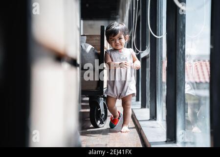 carino bambino che cammina in una scarpa accanto al bicchiere finestra Foto Stock