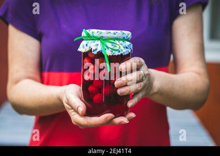 Donna che tiene in mano il composto di ciliegio. Frutta conservata in casa in vasetto di vetro. Foto Stock