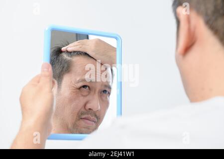 L'uomo medio-anziano asiatico guardava nello specchio e lo era Preoccupato per le molte rughe facciali causate da aging.Health care concetto Foto Stock