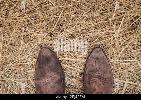 In piedi in stivali da cowboy su fieno d'oro. Vecchio stivale in pelle usurato. Direttamente sopra Foto Stock