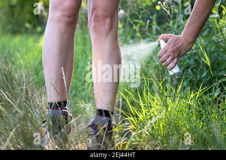 Repellente per zanzare. Donna che spruzzava repellente per insetti sulla gamba. Protezione della pelle contro zecche e altri insetti Foto Stock