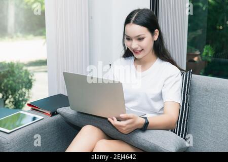 Bella giovane donna sorridente seduta sul divano e che lavora su un computer portatile. Foto Stock