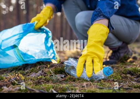 Inquinamento ambientale. Volontario raccogliendo bottiglia di plastica in foresta sporca. Rendi la Terra pulita! Primo piano con il guanto di protezione giallo indossabile a mano Foto Stock