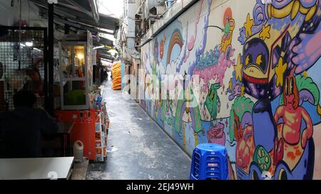 BANGKOK, THAILANDIA - 11 LUGLIO 2019: Cart alimentare vicino al muro graffiti sulla strada. Il cart del cibo si trova vicino alla parete colorata dei graffiti sul mercato sulla strada stretta. L Foto Stock