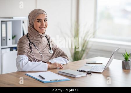 Positiva dottoressa seduta al banco di lavoro in clinica Foto Stock