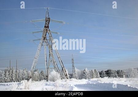 Un'incredibile combinazione della struttura in acciaio del traliccio della linea elettrica con fili tesi in primo piano e la foresta invernale all'orizzonte. Foto Stock