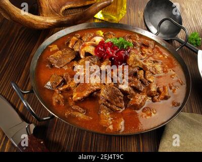 Selvaggina goulash di carne in una padella con mirtilli rossi su Legno di fondo Foto Stock