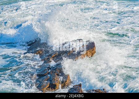 Un'immagine ravvicinata delle onde bianche che si spruzzi acquisite in movimento contro le rocce Foto Stock