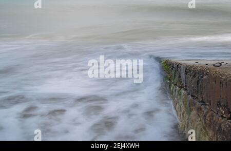 L'acqua schiumosa e lattiginosa si sfocia nel cielo al rallentatore mentre scende giù per uno scivolo nel mare spettrale di Swanage Bay, Dorset, Inghilterra Foto Stock