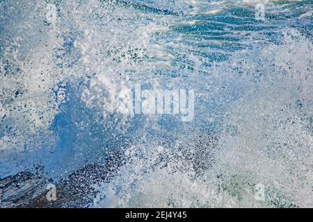Le onde che si infrangono contro le rocce costiere si incontrano in opposizione in un tuffo bianco schiumoso diagonale Foto Stock