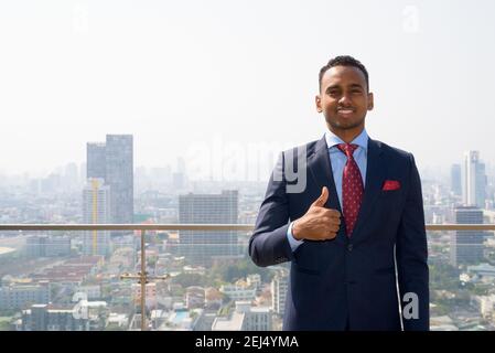 Ritratto di bel giovane uomo d'affari africano con vestito sorridente e. dare pollici in su Foto Stock