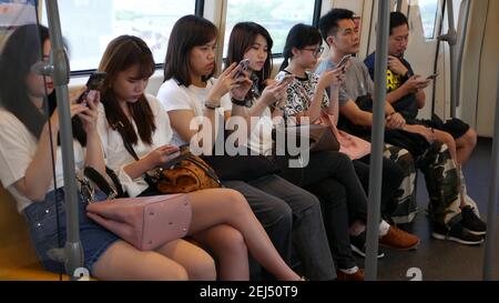 BANGKOK, THAILANDIA - 13 LUGLIO 2019: Passeggeri asiatici in treno con smartphone. Persone thailandesi online surfing internet in auto bts. Trasporti pubblici. Foto Stock