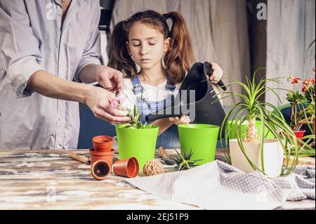 piccola bella ragazza sta innaffiare fiori per aiutare la madre con piantine. casa giardino, attività familiare. etnia caucasica. vista frontale. Foto Stock