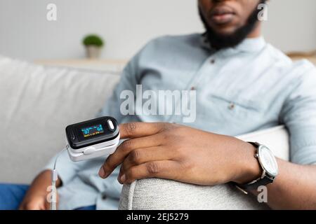 Black Man con pulsossimetro che misura la saturazione dell'ossigeno a casa Foto Stock