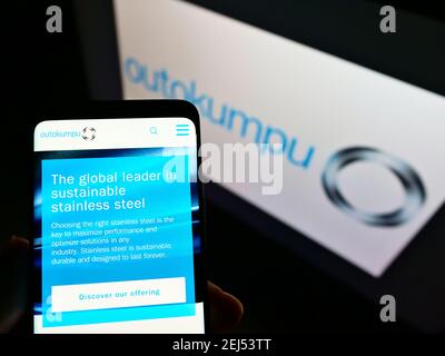 Persona che tiene il telefono mobile con il sito web del produttore finlandese di acciaio Outokumpu Oyj sullo schermo davanti al logo. Mettere a fuoco il centro del display del telefono. Foto Stock