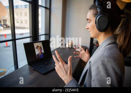 Ritratto di una donna d'affari millenaria concentrata durante una videochiamata di lavoro con il suo collega. Indossa le cuffie. Concetto di lavoro remoto. Foto Stock