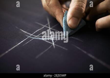 Tailor sta tracciando con il gesso il motivo sul tessuto su misura sarors a Savile Row, Londra, Regno Unito. Foto Stock