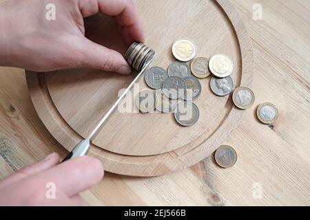Le mani tagliano una pila di monete in euro e dollaro con un coltello, separandole come pezzi di cibo su un tagliere. Concetto di tasse, frode o profitto. Foto Stock