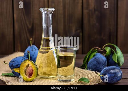 Brandy di prugne o schnapps in bicchieri e prugne fresche gustose su un tavolo di legno. Messa a fuoco selettiva. Foto Stock