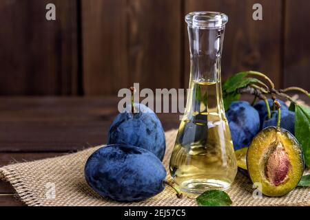 Brandy di prugne o schnapps in una piccola bottiglia di vetro con prugne fresche e gustose su un tavolo di legno. Messa a fuoco selettiva. Foto Stock