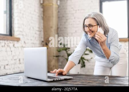 Donna d'affari di successo senior grigio-capelli donna in piedi in ufficio, rispondendo alla telefonata da parte di un dipendente o di un cliente Foto Stock