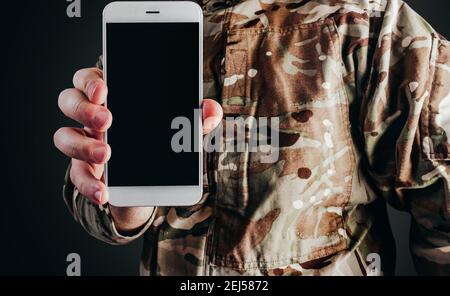 Foto del soldato in uniforme camuffata che tiene lo smartphone su sfondo nero. Foto Stock