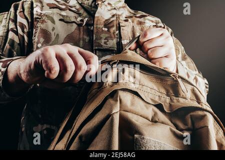 Foto del soldato in uniforme camuffata che tiene e sfreccia lo zaino su sfondo nero. Foto Stock