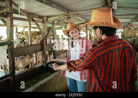 due allevatori di mucche indossano cappelli stanno chiacchierando con loro mani che indicano qualcosa nel capannone di bestiame nel sfondo Foto Stock