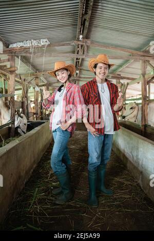 la coppia contadina si alza e sorride con un pollice in su nel ranch di bestiame penna Foto Stock