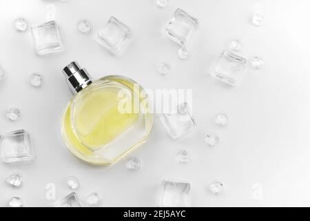 Bottiglia di profumo giallo femminile, Fotografia obiettivo di bottiglia di profumo in cubetti di ghiaccio e acqua su tavola bianca. Vista dall'alto. Foto prodotto mockup, con Foto Stock