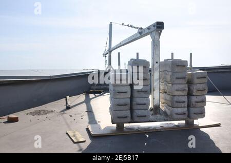 Contrappeso o bilanciamento del peso blocchi di calcestruzzo o mattoni come parte di una piattaforma di funi sospese per lavori di facciata su edifici ad alto livello multipiano. Uomo Foto Stock