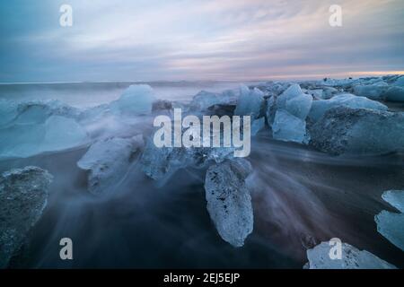 Ice rock con spiaggia di sabbia nera a Jokulsarlon spiaggia al tramonto. Spiaggia di diamante nel sud-est dell'Islanda. Foto Stock