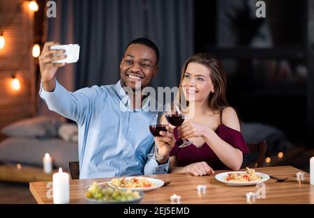 Data di residenza. Felice coppia interracial cena e presa selfie su smartphone Foto Stock
